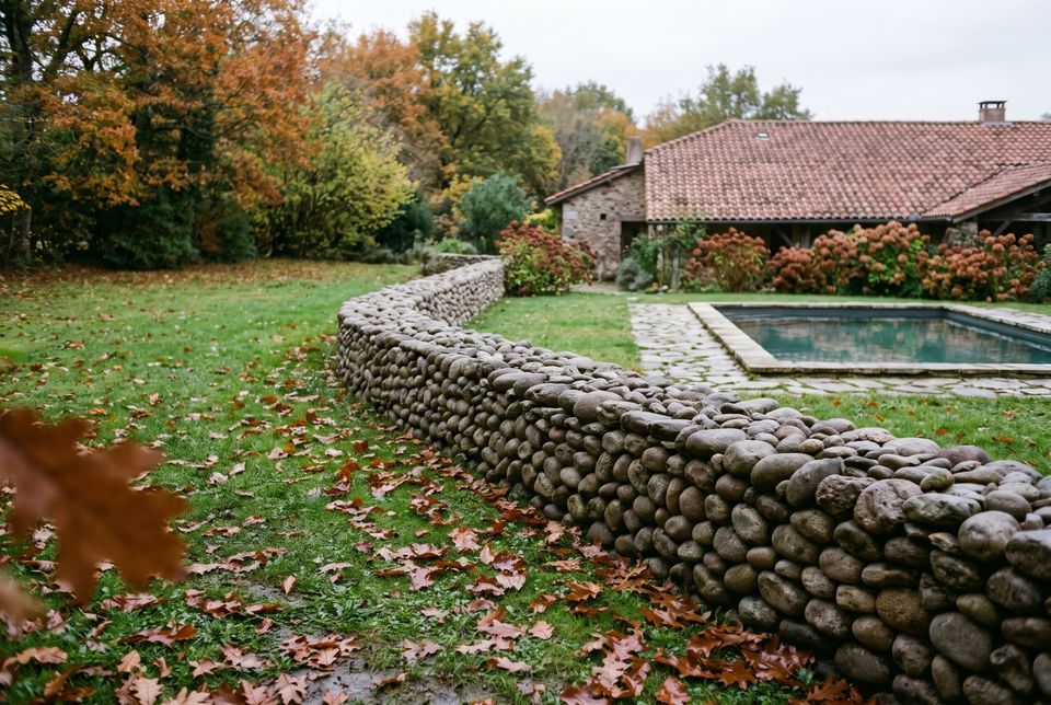 Muret de galets de rivière au bord d'un jardin humide, feuilles de chêne au sol